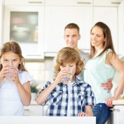 Boy and girl drinking water with lime in the kitchen while the parents are watching